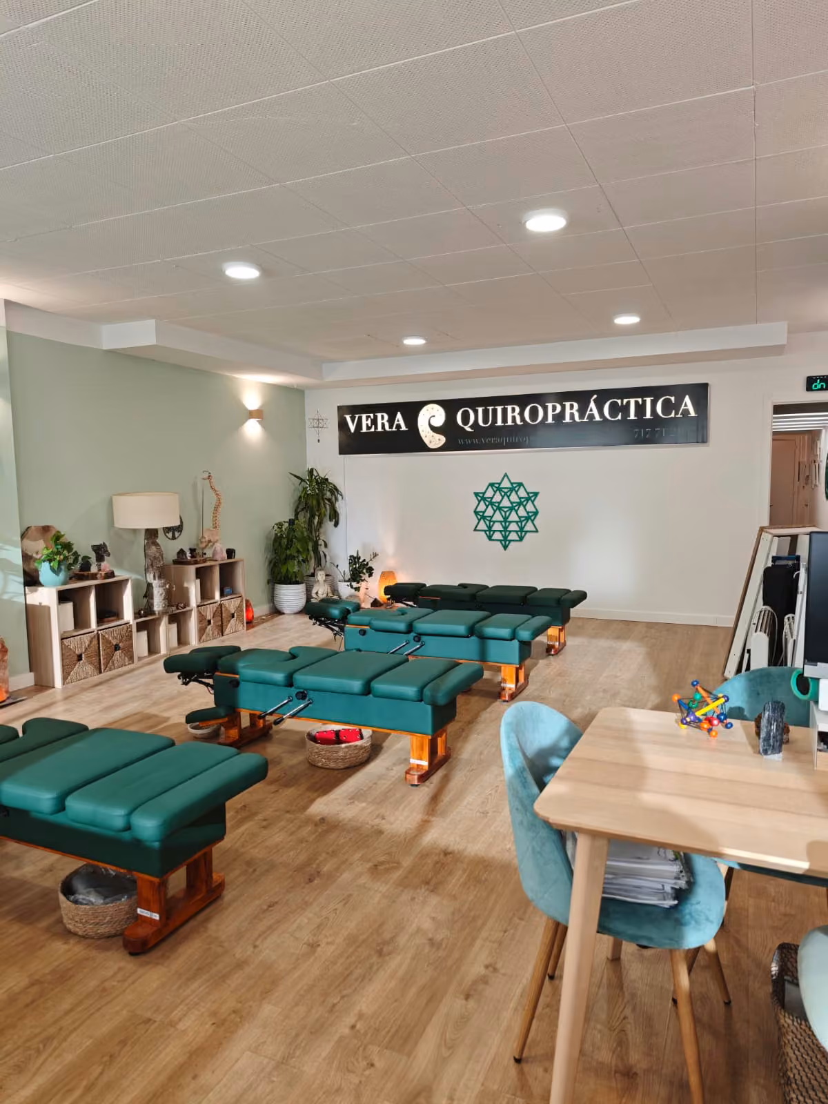 Sala de la consulta con las camillas de ajuste en verde y, al fondo, el rótulo de Vera Quiropráctica.